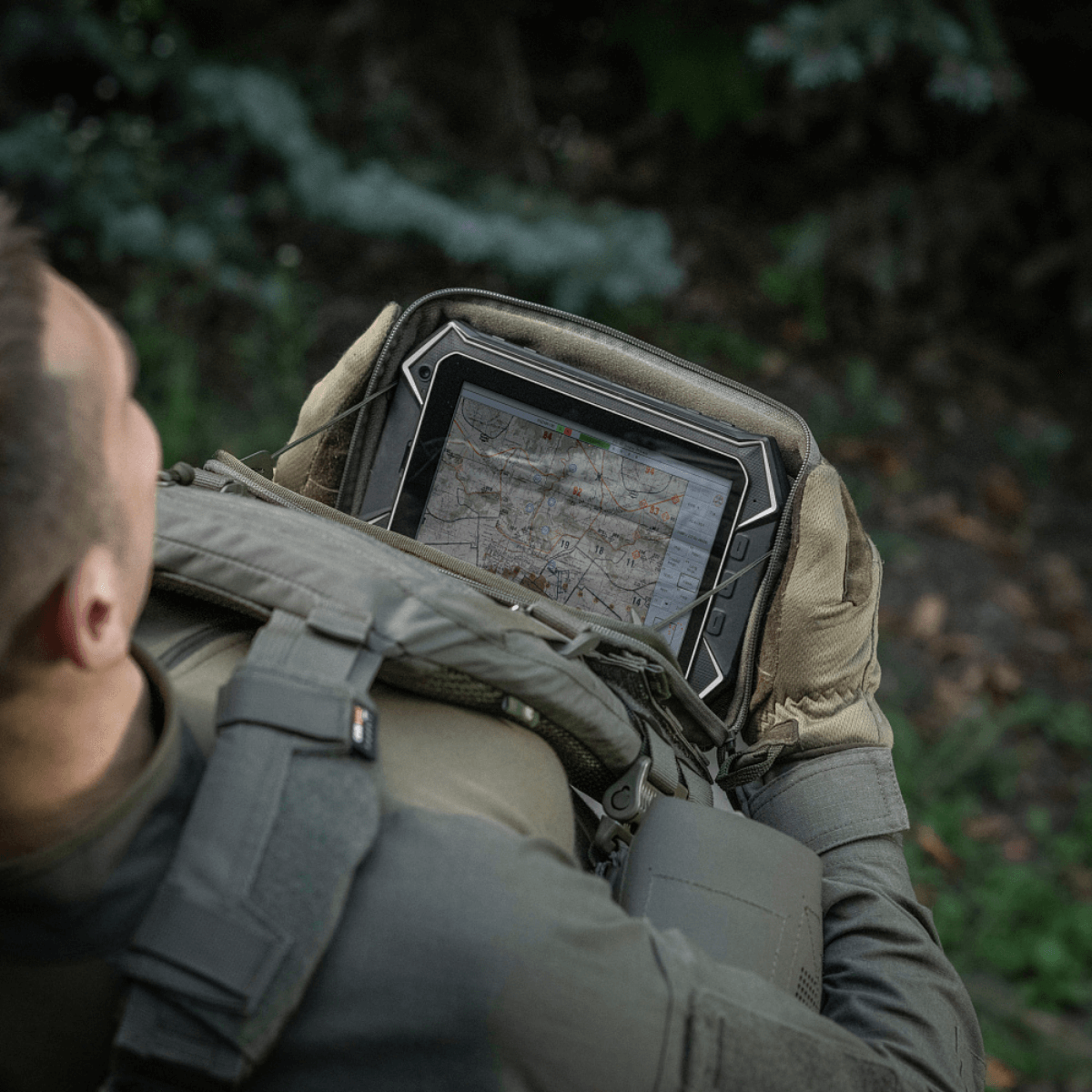 Henkilö, jolla on M-Tac Admin Pouch Large Elite, pitää tablettia metsässä.