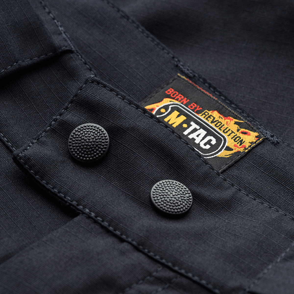 M-Tac Shorts Aggressor Gen.II Flex lähikuva kestävästä napituksesta ja logosta ripstop-materiaalissa Teflon-pinnoitteella, sopii harjoitteluun ja vapaa-aikaan.