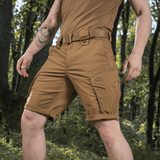 M-Tac Shorts Aggressor Gen.II Flex ruskeana ripstop-materiaalista, sopii harjoitteluun ja vapaa-aikaan, esitetty metsässä.