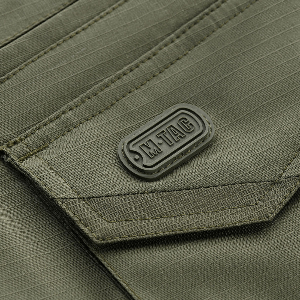Lähikuva M-Tac Shorts Aggressor Gen.II Flexin taskumuotoilusta vihreässä ripstop-kankaassa, taktinen ommel ja M-Tac-merkintä.