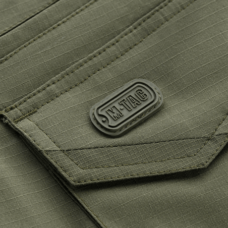 Lähikuva M-Tac Shorts Aggressor Gen.II Flexin taskumuotoilusta vihreässä ripstop-kankaassa, taktinen ommel ja M-Tac-merkintä.