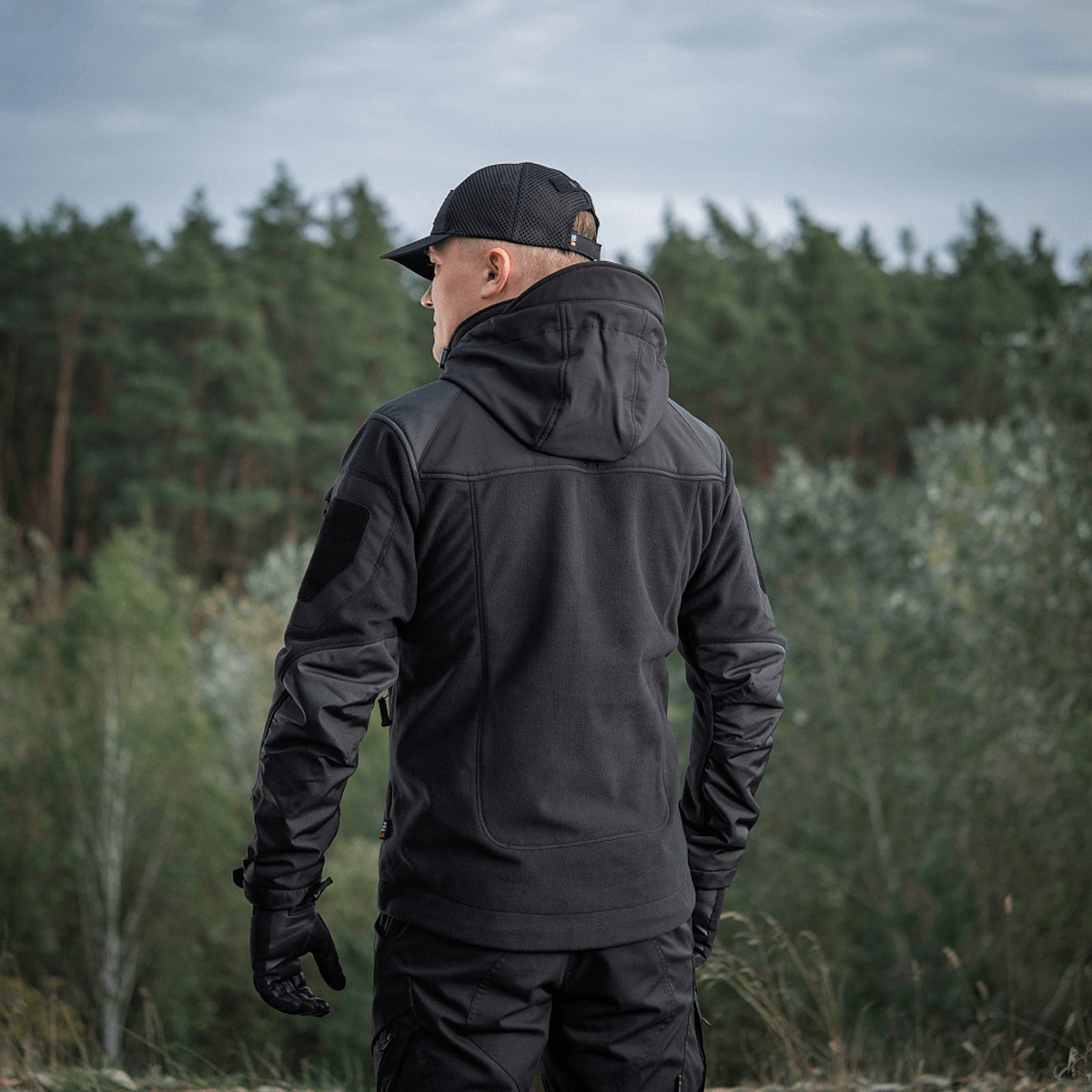 Henkilö pukeutuneena M-Tac Norman Windblock -fleecetakkiin luonnossa, takaa nähtynä.