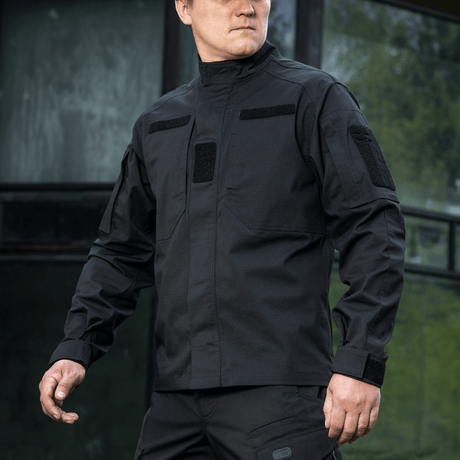 Mies pukeutuneena mustaan M-Tac Patrol Flex -takkiin velcro-paneeleilla, piilotetuilla rintataskuilla ja tuuletusrei'illä taktista käyttöä varten