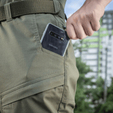 Henkilö ottaa puhelimen taskusta M-Tac Tactical Bukser Patrol Gen II Flex -housuissa ulkona.