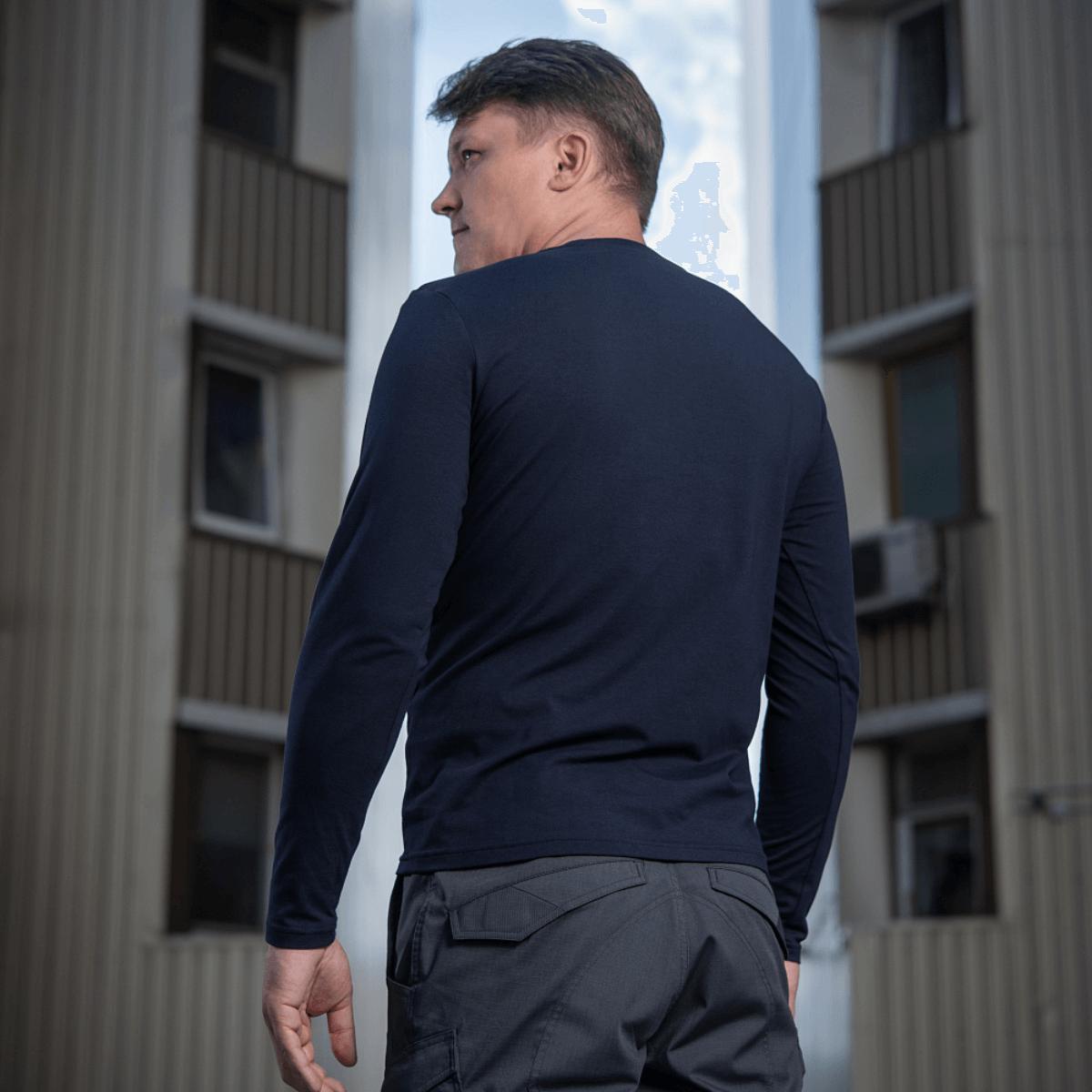 M-Tac Long-sleeve T-shirt 93/7 tummansinisenä, nähtynä takaa miehellä kaupunkiympäristössä.