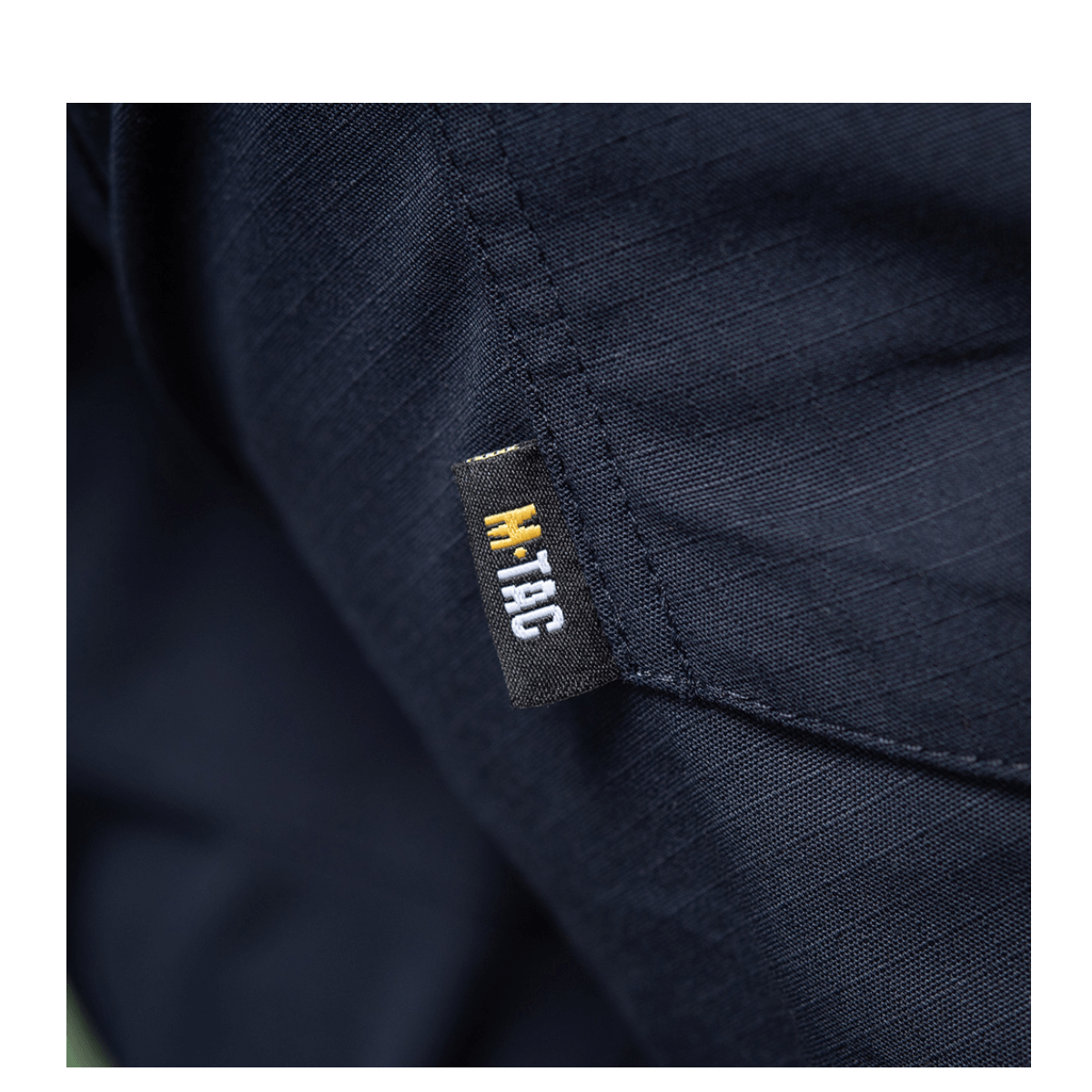 Yksityiskohta M-Tac Bukser Aggressor Dame Flex -housuista, M-Tac-logo tummansinisellä kankaalla.