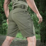 M-Tac Shorts Rubicon Flex tummanoliivinvihreät, cargotaskut, takaapäin ulkoilmassa nähtynä, sopivat kesään ja maks. liikkumavapauteen.