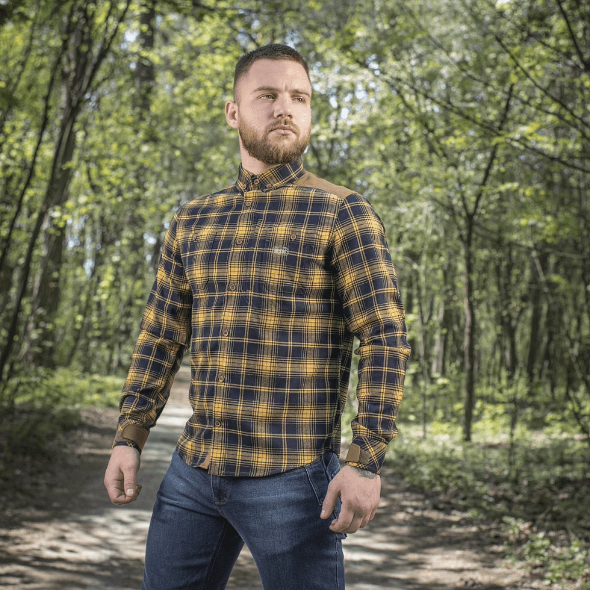 Mies M-Tac Redneck -paidassa navy sininen/keltainen metsäympäristössä. Klassinen ruutumuotoilu ja säädettävät hihat, sopii vapaa-aikaan.
