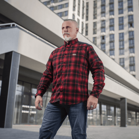 Mies pukeutuneena M-Tac Redneck -paitaan punamustassa ruutukuosissa urbaanissa taustassa, taktinen muotoilu, sopii työhön ja vapaa-aikaan.