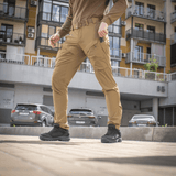 Mies pukeutuneena M-Tac Rubicon Flex -housuihin kaupunkiympäristössä, sopivat harjoitteluun ja vapaa-aikaan, valmistettu 4-Way Stretch -kankaasta mukavuutta ja liikettä varten.