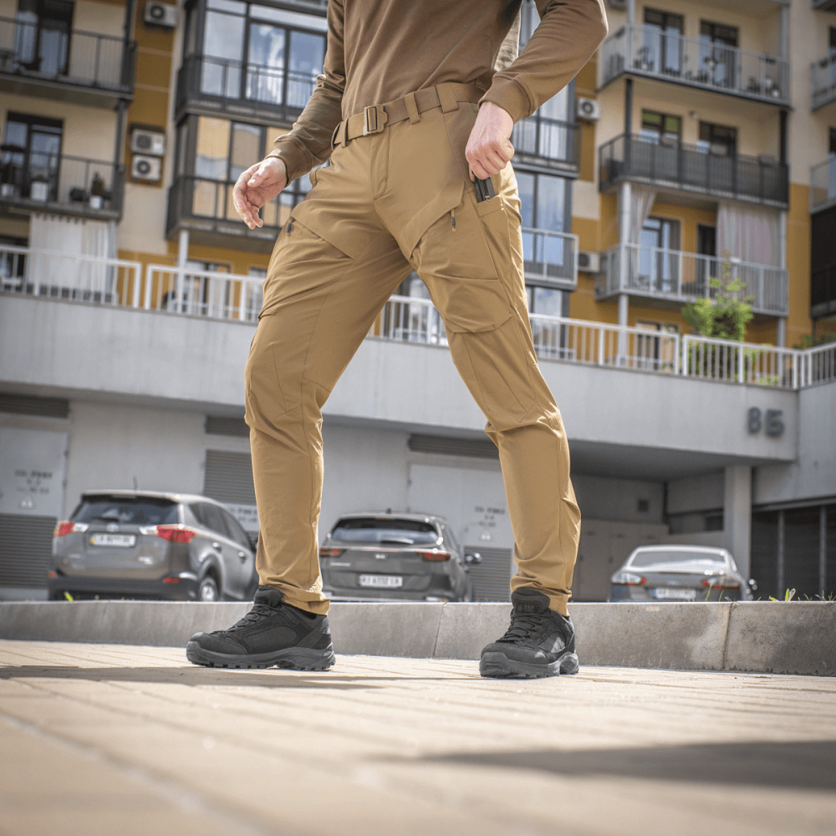 Mies pukeutuneena M-Tac Rubicon Flex -housuihin kaupunkiympäristössä, sopivat harjoitteluun ja vapaa-aikaan, valmistettu 4-Way Stretch -kankaasta mukavuutta ja liikettä varten.