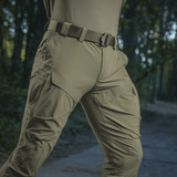 Henkilö esittelee M-Tac Rubicon Flex -housuja nylon/spandex-sekoitteesta, cargo-taskut, sopivat aktiviteetteihin kuten treeni ja vapaa-aika.