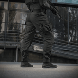 Mies pitää yllä M-Tac STURM NyCo Extreme Gen.II -housuja joustavilla inserteillä, suunniteltu taktiseen käyttöön, kuvattu ulkona.