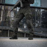 Mies käyttää M-Tac STURM NyCo Extreme Gen.II -housuja aseen kanssa modernin rakennuksen edessä.