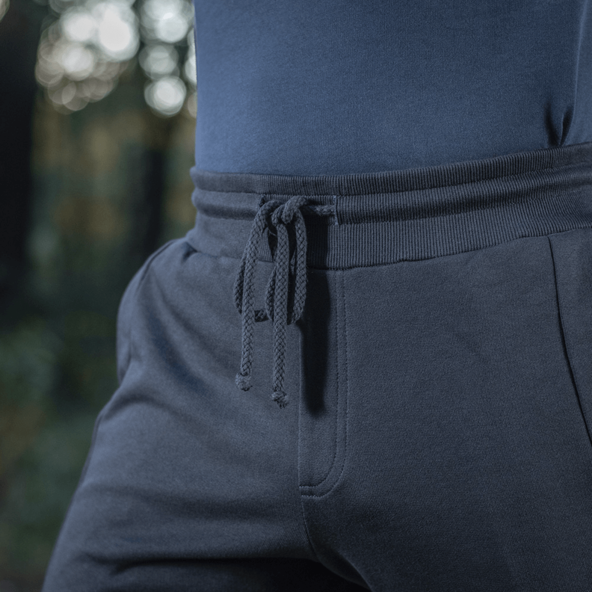 Henkilö pukeutuneena M-Tac Stealth Cotton -housuihin kuminauhalla vyötäröllä ja sivutaskuilla, valmistettu 100% puuvillasta mukavuuteen ja liikkumisvapauteen.