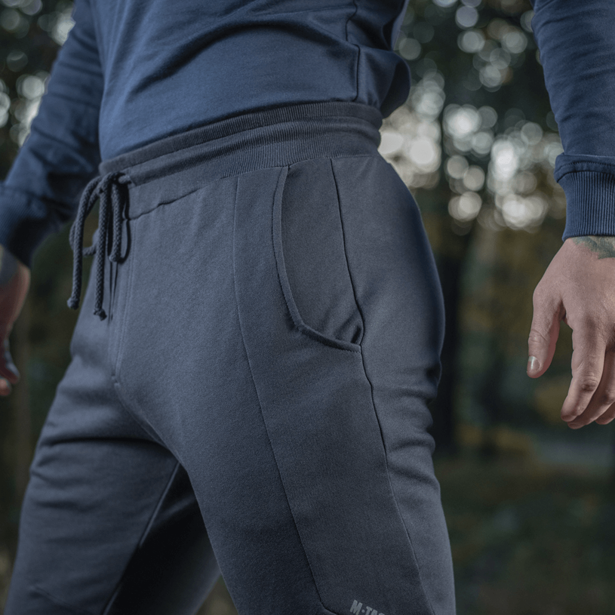 Mies pukeutuneena M-Tac Stealth Cotton -housuihin urheiluun ja arkeen, lähikuva, korostaa mukavuutta ja tyylikästä muotoilua.