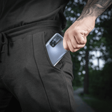Mies pukeutuneena M-Tac Shorts Casual Fit Cotton -shortseihin, puhelin taskussa, esittelee käytettävyyden ja muotoilun.
