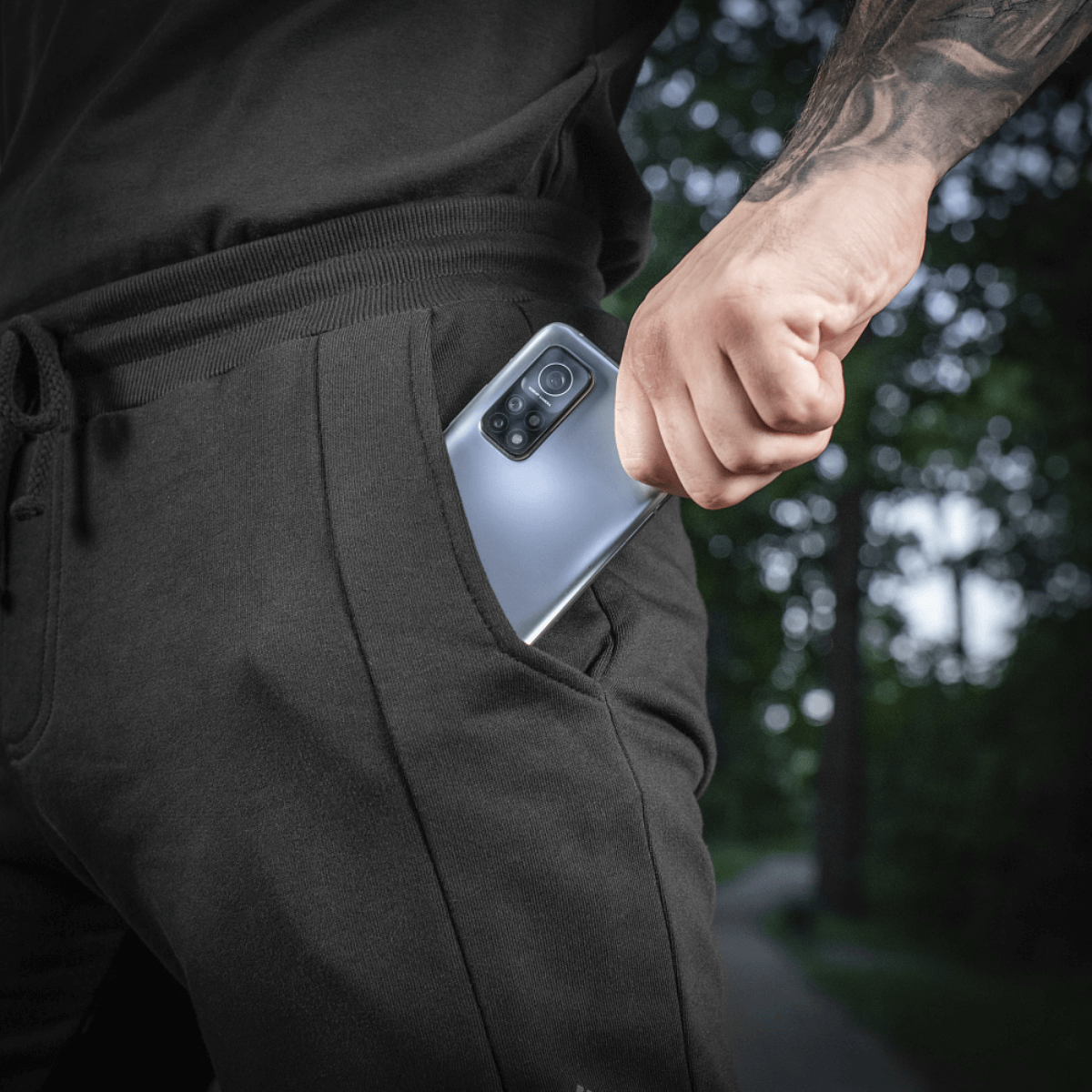 Mies pukeutuneena M-Tac Shorts Casual Fit Cotton -shortseihin, puhelin taskussa, esittelee käytettävyyden ja muotoilun.