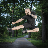 Mies hyppää puistossa M-Tac Shorts Casual Fit Cotton -shortseissa, rento musta asu, valmistettu hengittävästä 100 % puuvillasta.