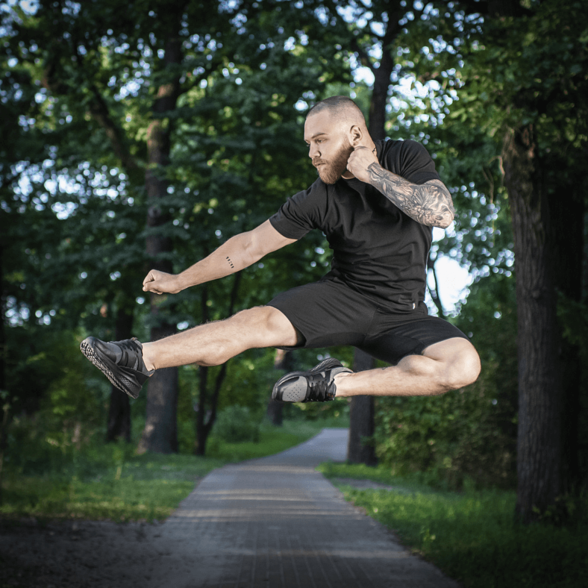 Mies hyppää puistossa M-Tac Shorts Casual Fit Cotton -shortseissa, rento musta asu, valmistettu hengittävästä 100 % puuvillasta.