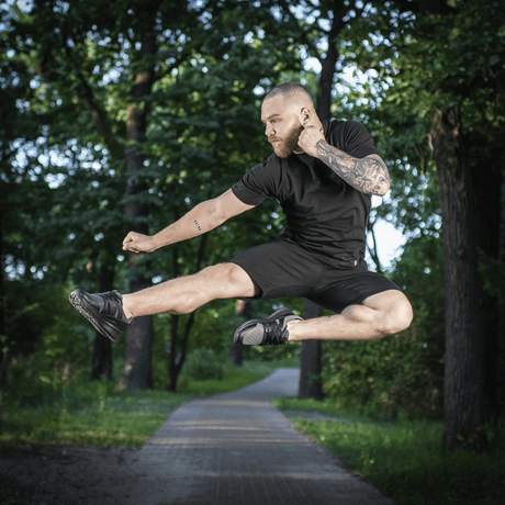 Mies hyppää puistossa M-Tac Shorts Casual Fit Cotton -shortseissa, rento musta asu, valmistettu hengittävästä 100 % puuvillasta.