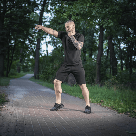 Mies metsässä M-Tac Shorts Casual Fit Cotton -shortseissa, näyttää liikkuvuuden ja pelkistetyn muotoilun puupolulla.