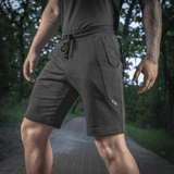 Mies pukeutuneena M-Tac Shorts Casual Fit Cotton -shortseihin, mustat taskuilla ja kuminauhalla vyötäröllä, ihanteelliset aktiiviseen käyttöön, 100% puuvillaa.