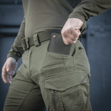Mies pukeutuneena M-Tac Bukser Patriot Gen.III Vintage -housuihin esittelee taskujen toiminnallisuutta ulkona.
