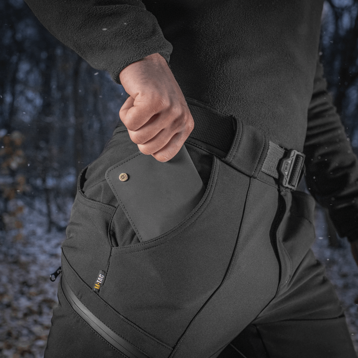 M-Tac Bukser Soft Shell Vinter mustana, fleece-vuori, mies laittaa älypuhelinta taskuun, sopii kylmiin olosuhteisiin.