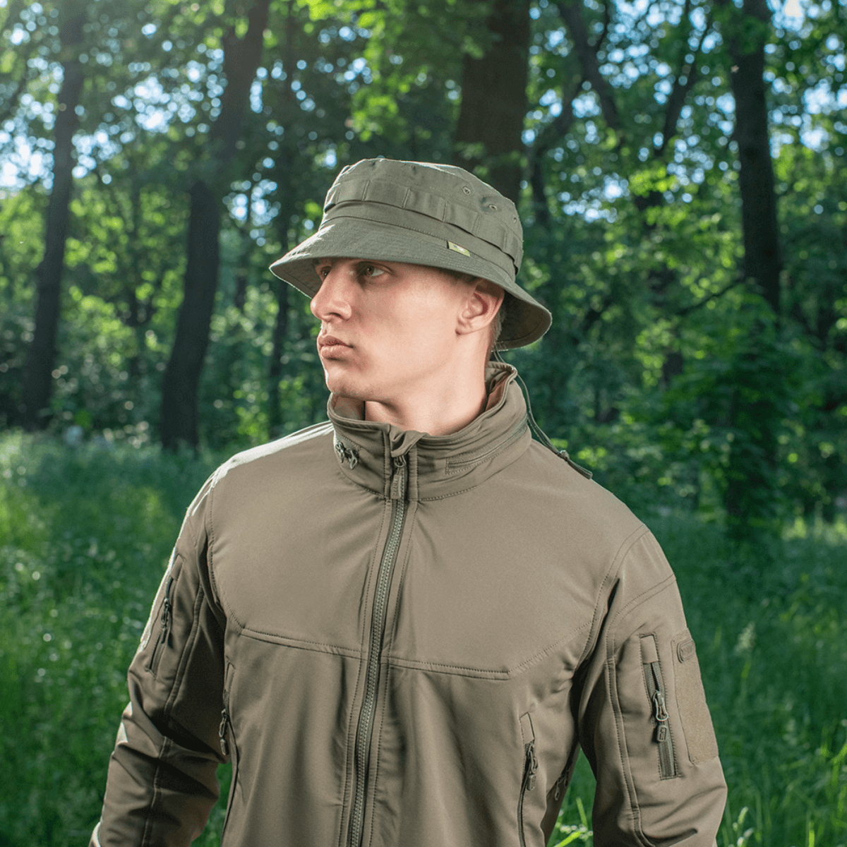 Mies, joka käyttää M-Tac Panama Rip-Stop army-hattua puolijäykkällä lipalla ja ilmanvaihtoaukoilla, seisoo metsässä. Boonie-mallin innoittama.
