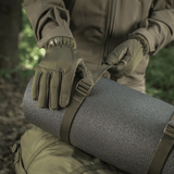 Henkilö käyttää M-Tac puristusremmiä kiinnittämään varusteita reppuun metsässä, käytännöllinen vaelluksilla ja sotilaskäytössä.