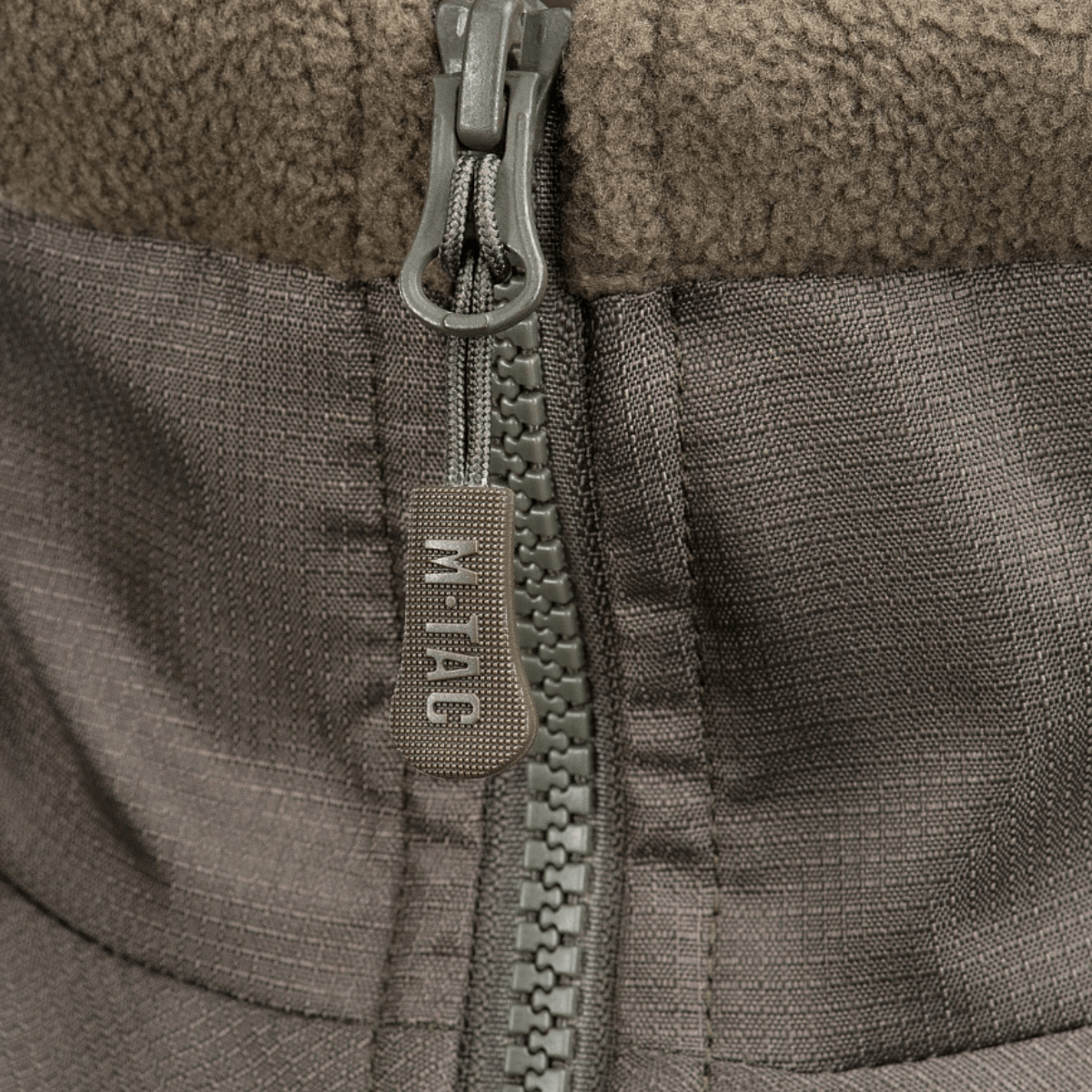 Vetoketjun yksityiskohta M-Tac Alpha Microfleece takki Gen.II:stä, suunniteltu taktiseen käyttöön ja ulkoilma-aktiviteetteihin kylmässä säässä.