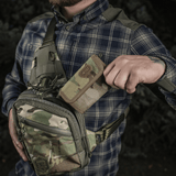Mies pitelee M-Tac Pung Elite Gen.II:tä Cordura 500D:stä maastorepun vieressä ulkoilmassa.