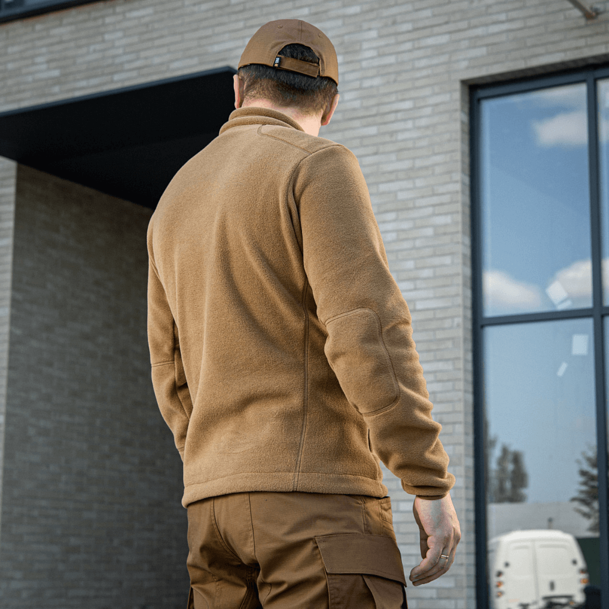 Mies M-Tac Nord Polartec -fleecetakissa ruskeana rakennuksen edessä.