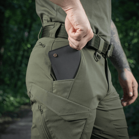 Mies pukeutuneena M-Tac Aggressor Summer Flex Shorts -shortseihin metsässä, käsi taskussa näyttää puhelimen säilytyksen. Tuoteavainsana: M-Tac Aggressor Summer Flex Shorts.