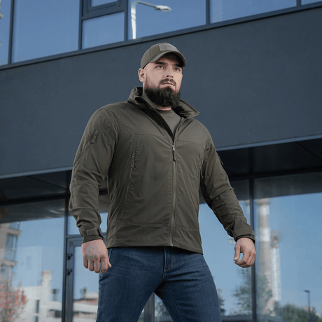 Mies pukeutuneena M-Tac Flash -takkiin rakennuksen edessä, monikäyttöinen retkeily- ja urheilutakki, käytännöllinen kevyt malli ilman tarrapaloja