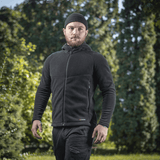 Mies pukeutuneena M-Tac Sprint Fleece Sweatshirt Polartec mustana, seisoo ulkona puiden edessä.