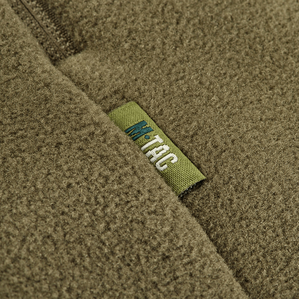 Lähikuva M-Tac Sprint Fleece Sweatshirt Polartec -etiketistä oliivinvihreällä fleece-kankaalla.