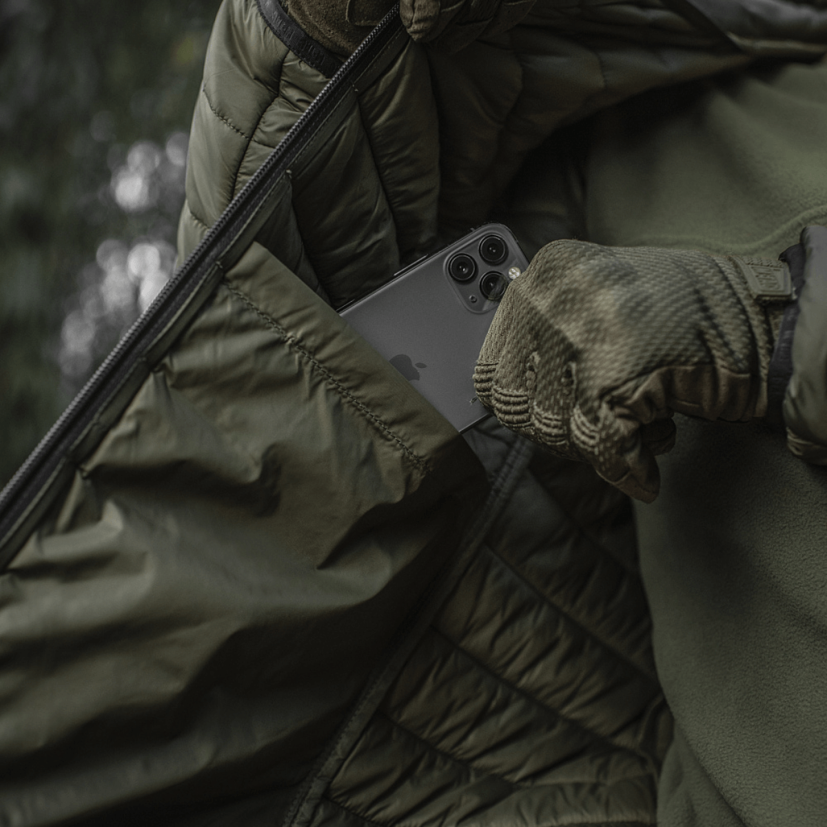 Henkilö M-Tac Stalker Gen.III -takissa, puhelin taskussa, säätää takkia, näyttää tyyliä ja toiminnallisuutta.