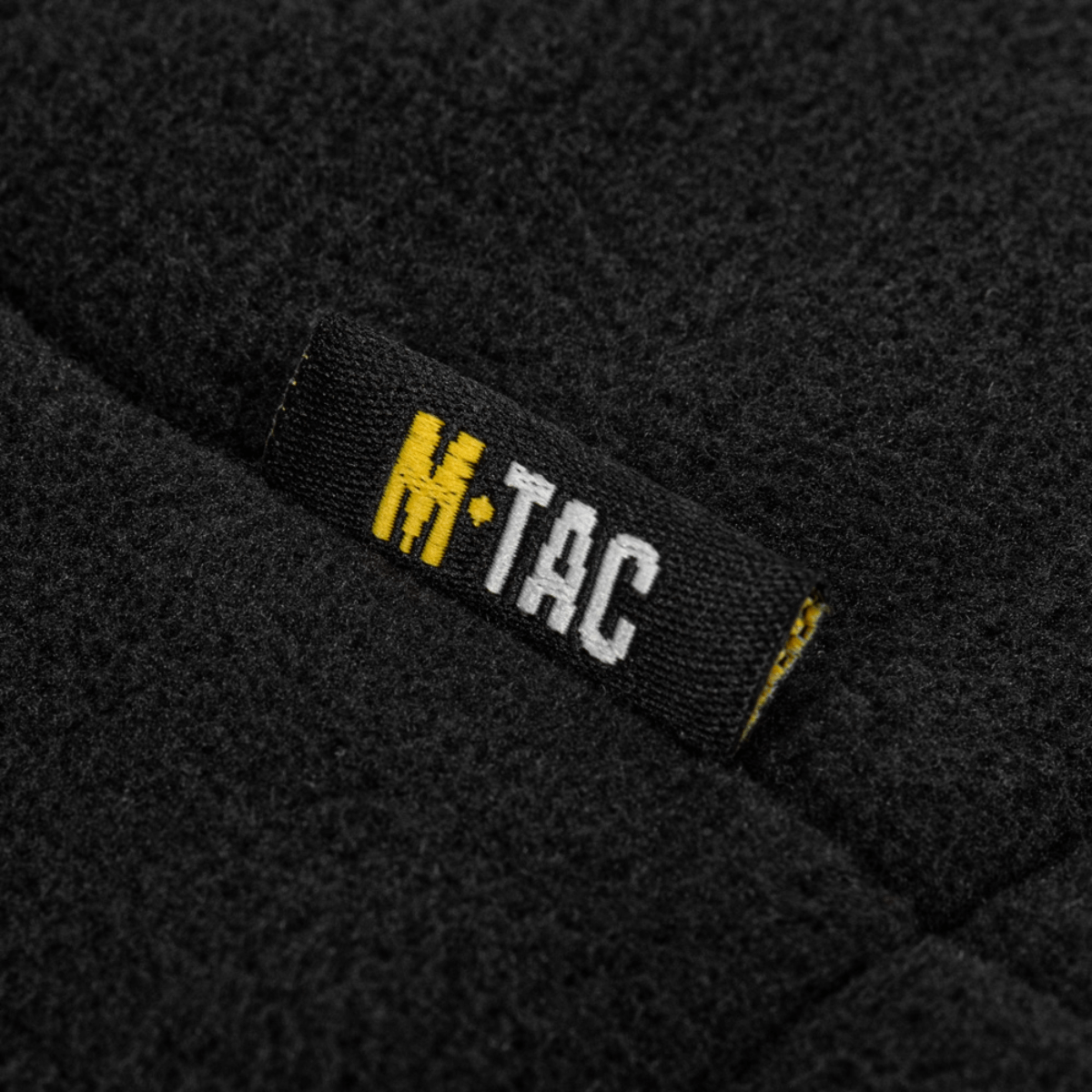 Lähikuva M-Tac Combat Fleece Polartec -takista, musta Polartec-fleece ja M-Tac-logo.