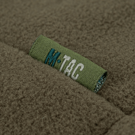 M-Tac Combat Fleece Polartec -takki, fokusoitu merkki hihassa, näyttää tekstuurin ja brändilogon yksityiskohdat.