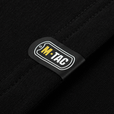 Lähikuva M-Tac-logosta M-Tac Raglan Odin Mystery -paidassa mustassa kankaassa, näyttää muotoilun ja materiaalin.