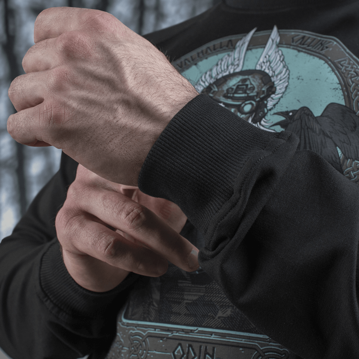 Mies säätää M-Tac Raglan Odin Mystery -paidan hihaa Odin-kuviolla, valmistettu miellyttävästä puuvilla-elastaanikankaasta, sopii arkeen.