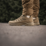 M-Tac Tactical Sneakers IVA henkilöllä ruskeiden housujen kanssa, kevyet ja tuulettuvat kengät, täydelliset kesäaktiviteetteihin ja ulkokäyttöön.