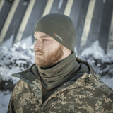 Mies pukeutuneena harmaaseen M-Tac Fleece Watch Cap Light Polartec -pipoon lumisessa maisemassa, yllään maastokuvioista vaatetusta, sopii talvisäähän.
