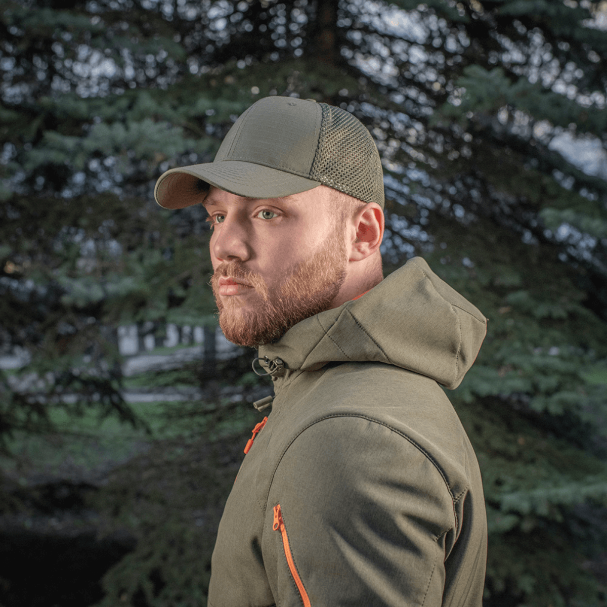 Mies seisoo ulkona puun edessä, M-Tac Mesh Flex Ripstop Baseball Cap en vihreänä.