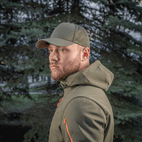 Mies seisoo ulkona puun edessä, M-Tac Mesh Flex Ripstop Baseball Cap en vihreänä.