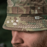 Lähikuva M-Tac Panama Hat Gen.II NYCO:sta, camo-kuvio, esittelee kestävää NYCO-kangasta ja MOLLE-liitäntää, päällä henkilö ulkona.