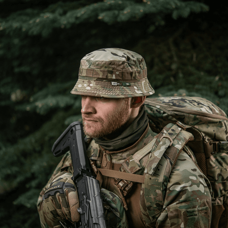 Mies pukeutuneena M-Tac Panama Hat Gen.II NYCO camo-designiin, sopii ulkoiluun ja sotilastyyliin, repun kanssa metsässä.