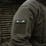 M-Tac Cat Eyes 3D PVC-patch takinhihassa taktillisessa ympäristössä, näyttää heijastavan ja fluoresoivan designin, kiinnitetty Velcrolla.